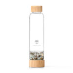 Eine Glas-Trinkflasche mit Bambusdeckel und einem separaten, mit Fluorit- und Tigerauge-Edelsteinen gefüllten Boden.