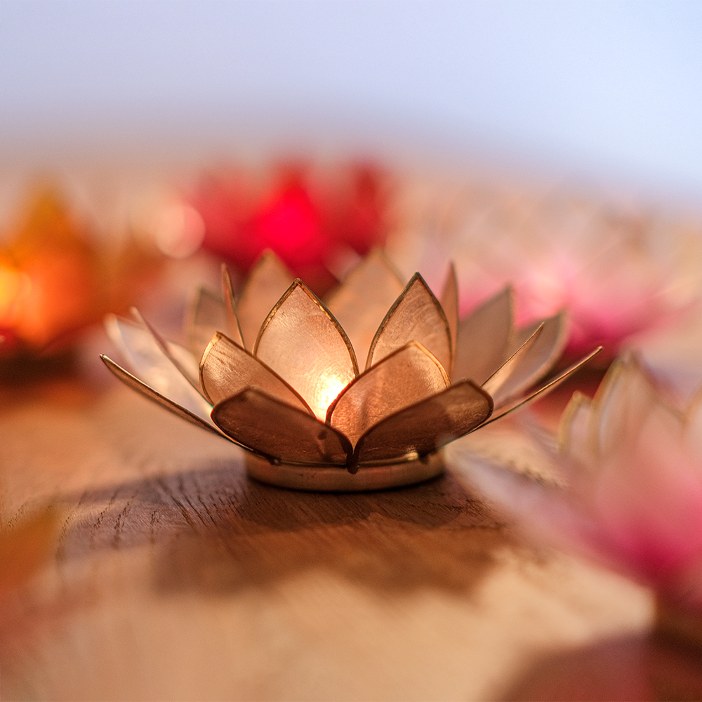 Ein Teelichthalter in Form einer goldenen Lotusblüte mit brennender Kerze schafft eine warme, gemütliche Atmosphäre auf einem Holztisch.