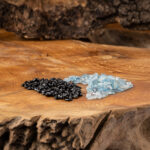 Eine Komposition aus glänzenden, schwarzen Obsidian- und hellblauen Aquamarin-Kristallsteinen, arrangiert auf einer rustikalen Holzoberfläche.