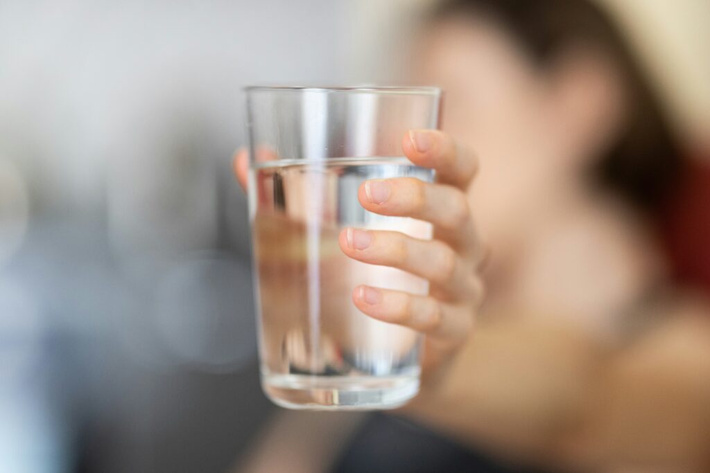 Eine Hand hält ein Glas mit klarem, reinem Wasser in die Kamera, um die Bedeutung von sauberem Trinkwasser zu verdeutlichen.