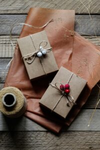 Zwei in naturbraunes Papier verpackte Geschenke, dekoriert mit Beeren und Schnur, liegen auf einem rustikalen Holztisch.