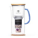 Eine Glaskaraffe mit einem mehrstufigen Wasserfilter, der Aktivkohle, Mineralien und Edelsteine enthält, ausgestattet mit einem Holzdeckel und einem blauen Griff.