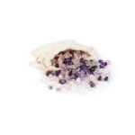 Eine Mischung aus Amethyst-, Rosenquarz- und Bergkristall-Edelsteinen, die aus einem kleinen Stoffbeutel auf eine weiße Fläche fallen.